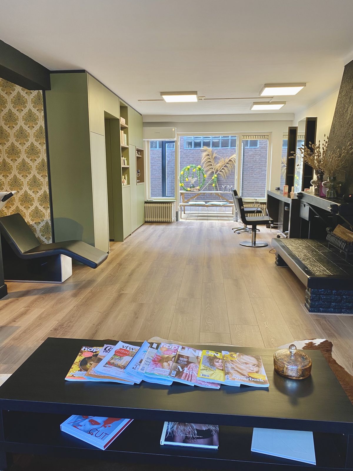 Het interieur van Kapsalon Juuds: olijfgroene wanden, damastbehang, een houten vloer en de kappersstoel