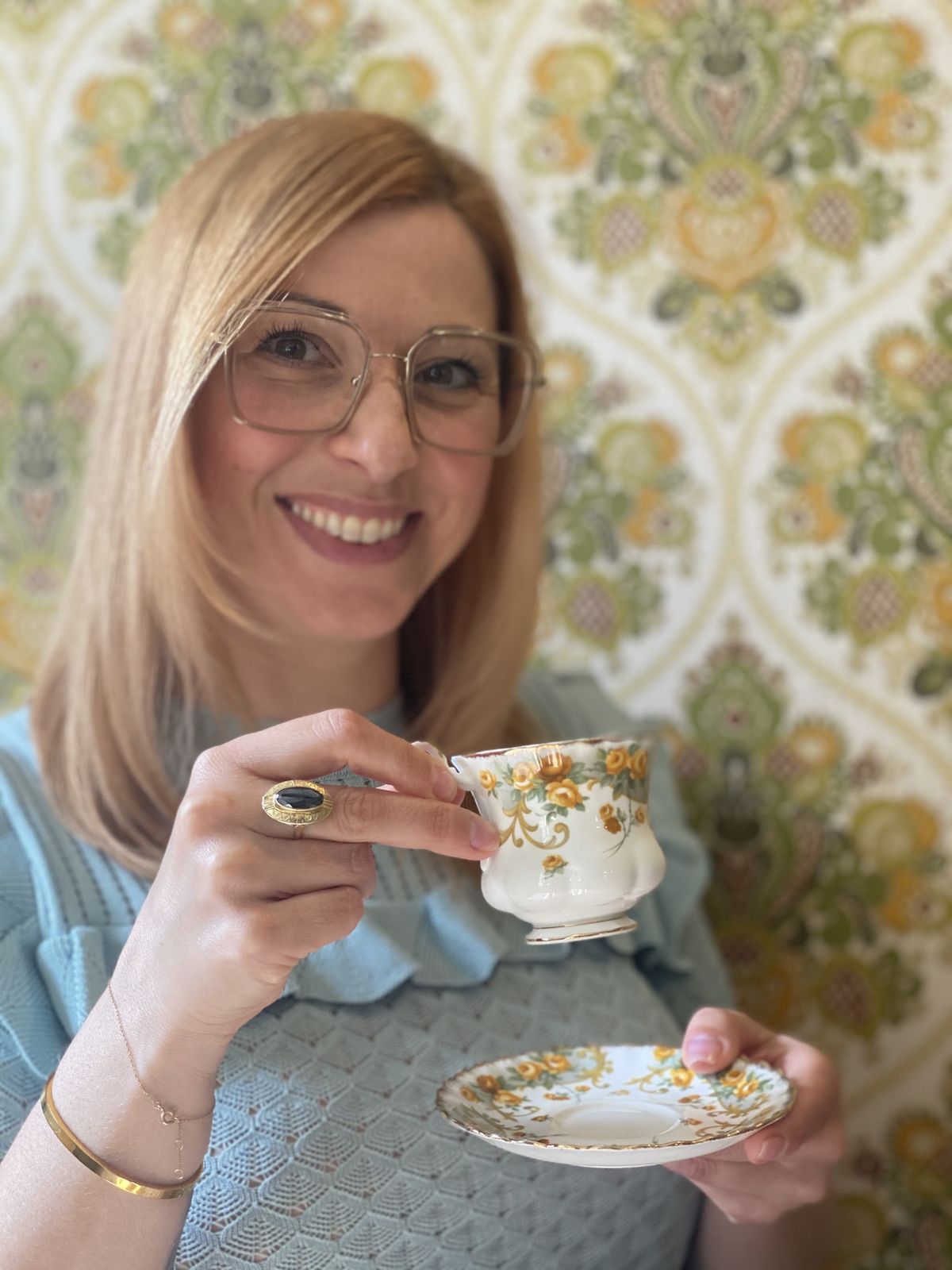 Een lachende vrouw met een vintage kopje thee voor het groen-gouden damastbehang in de salon